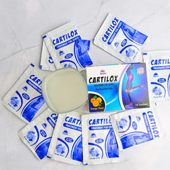 Phlox Cartilox joint supplement sachets, orange flavor, arranged with a glass of drink